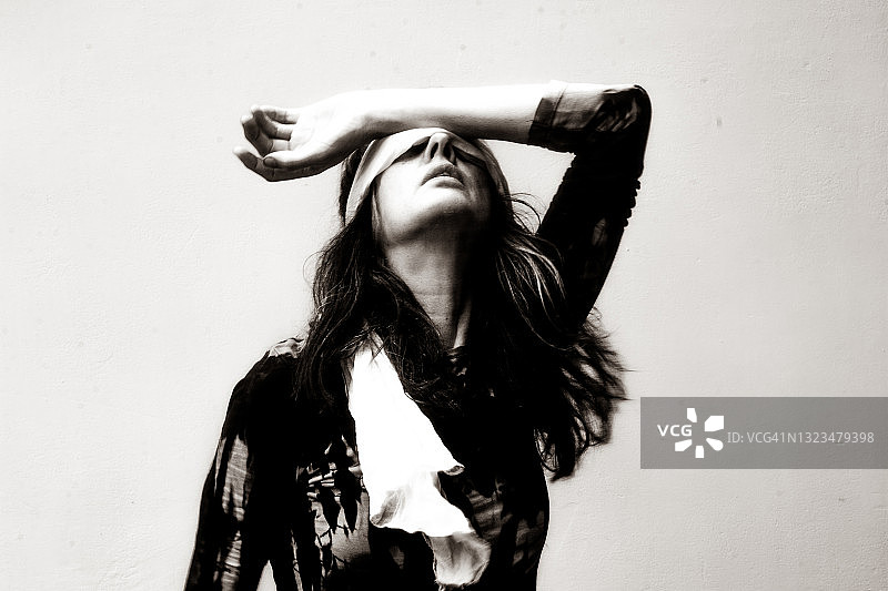 蒙着眼睛，手放在头顶的女人肖像。黑白照片，负面情绪图片素材