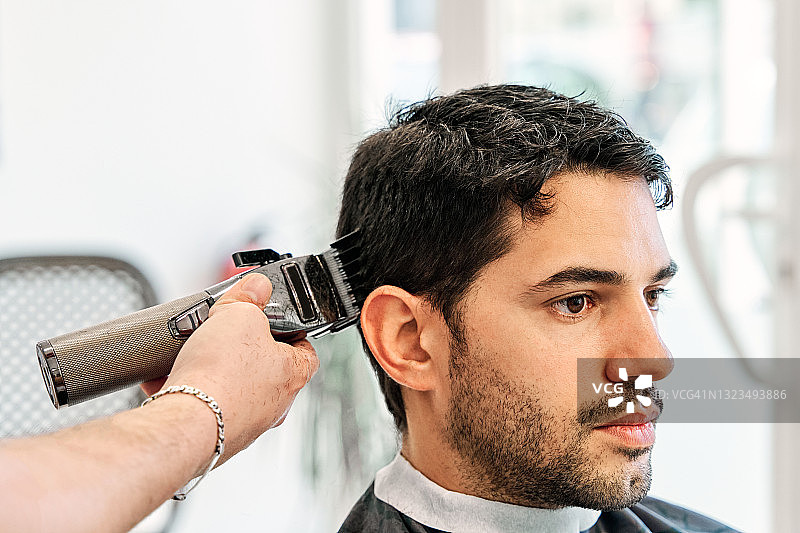 理发师在理发店用理发器给年轻人理发。图片素材