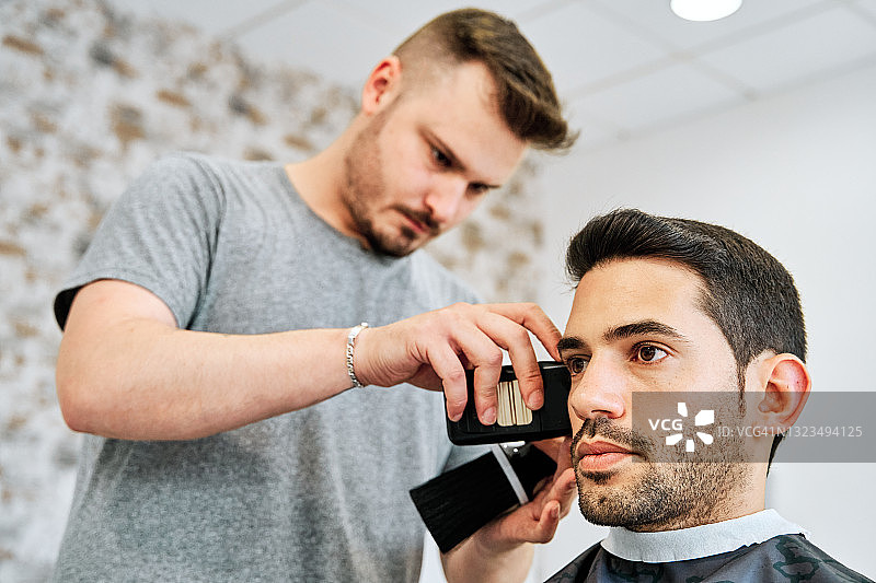 理发店内，年轻理发师为年轻男人修剪鬓角图片素材