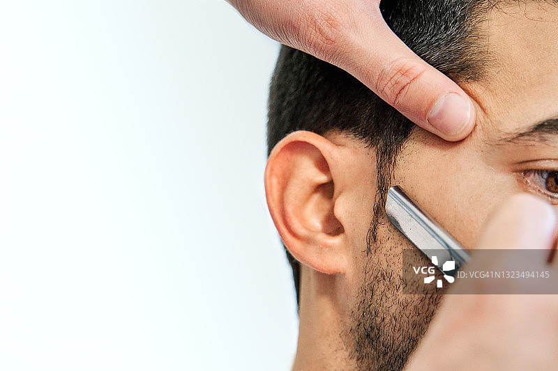 理发师用剃刀为年轻男子刮胡子的细节图片素材