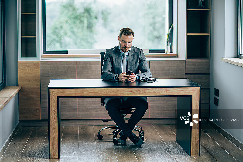 自信的商务人士在现代办公室使用智能手机图片素材