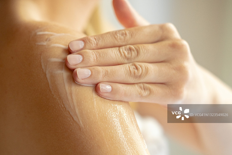 年轻女子肩部涂抹润肤露，进行身体皮肤护理图片素材