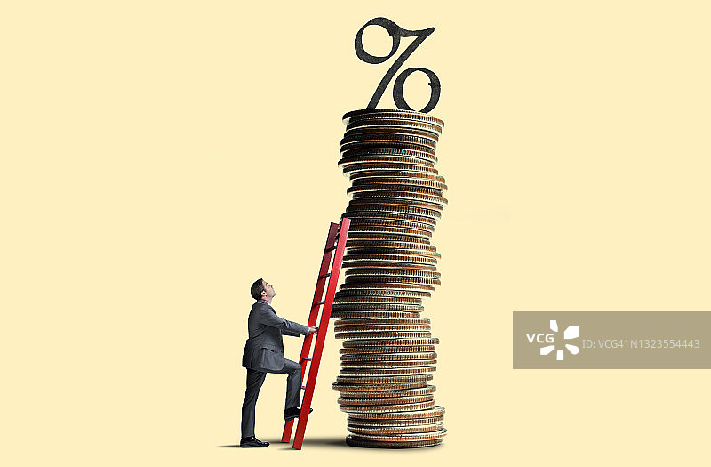 男人将梯子靠在顶部有利率符号的高大硬币堆上图片素材