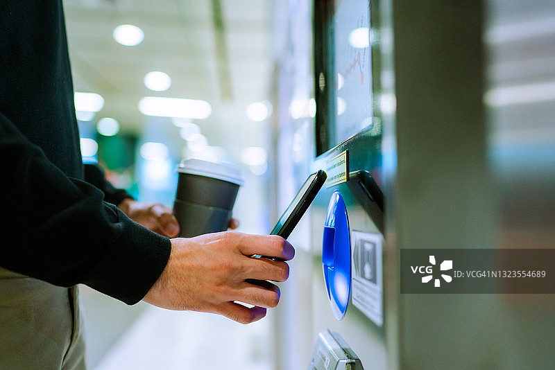 特写：一位年轻的亚洲男人在地铁自助结账机上使用智能手机进行非接触式支付图片素材