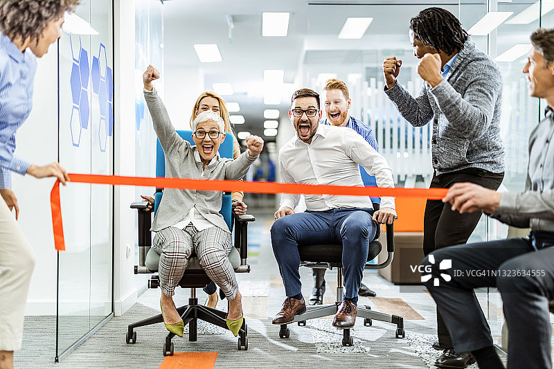 办公室里玩椅子赛跑的快乐同事图片素材