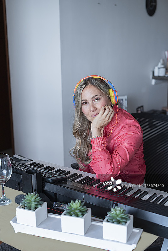 一位美丽的钢琴老师正在上网课，她看着镜头微笑，并用耳机教学的肖像图片素材