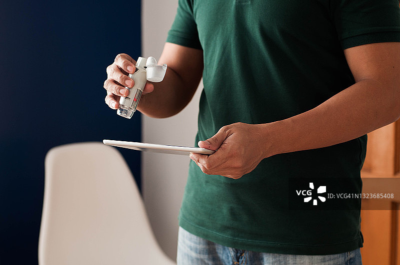拿着哮喘吸入器和数位平板电脑的东南亚青年男子腰部特写图片素材