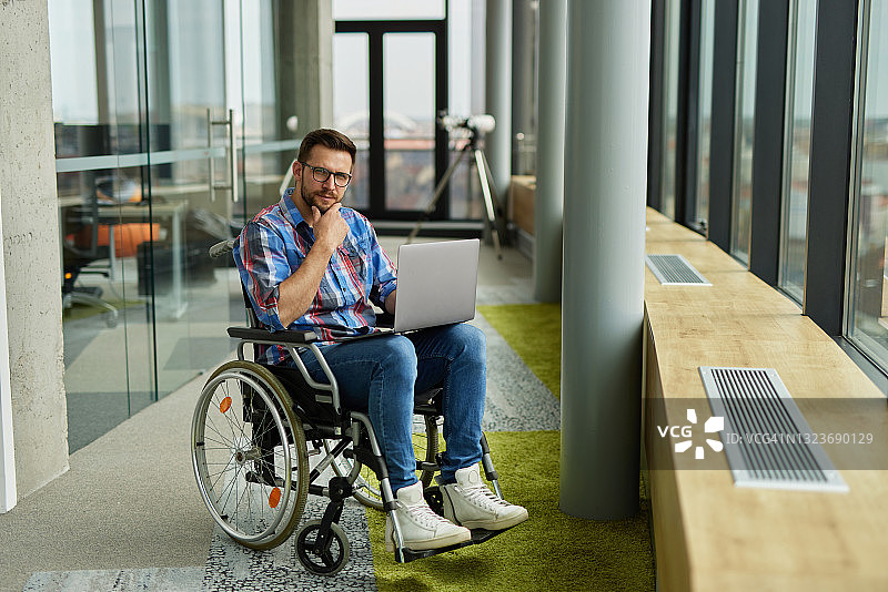 坐在轮椅上使用笔记本电脑的残疾男性IT工作者图片素材