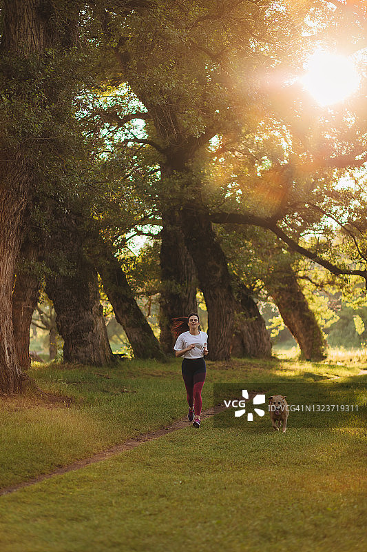 年轻女运动员在户外跑步，可爱的狗狗陪伴左右图片素材