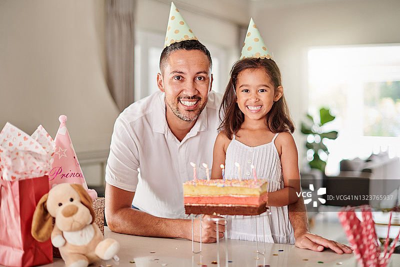 小女孩和父亲戴着派对帽站在生日蛋糕前图片素材
