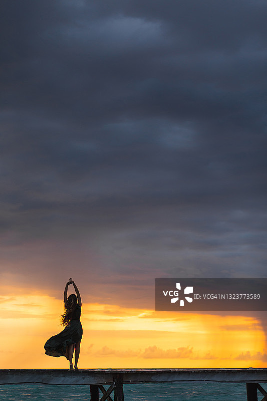 彩色夕阳下木制码头上看海的女人剪影图片素材