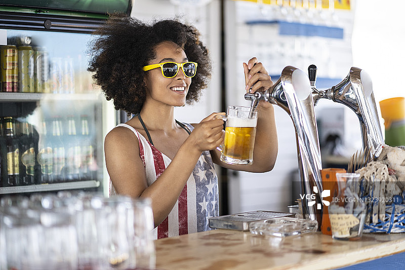 漂亮的非裔美国酒保倒着啤酒，戴着墨镜图片素材