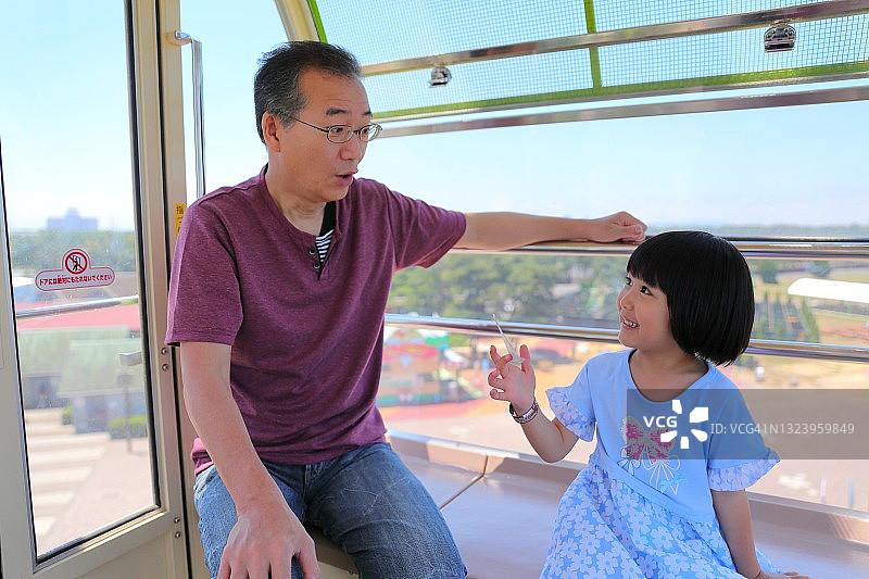 父亲和孩子在海边游乐园的摩天轮上交谈图片素材