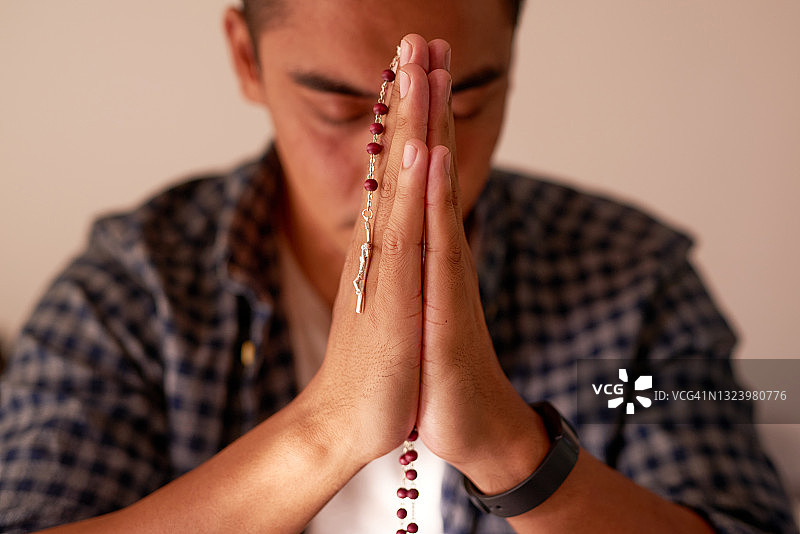 年轻帅气的男人独自在家祈祷时使用念珠图片素材