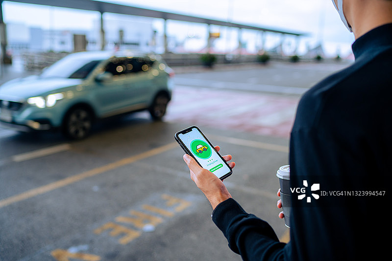 时尚亚洲青年在城市街道使用手机App订出租车图片素材