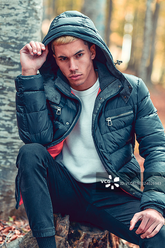 坐在森林树桩上的穿夹克的现代男人图片素材