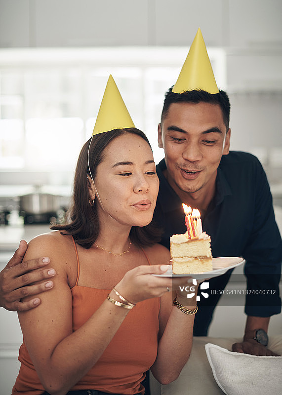 年轻情侣在家中吹灭蛋糕上的蜡烛图片素材