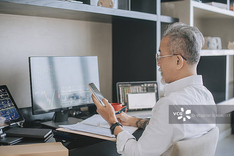 中国年长男子在家工作，多台电脑监控股市图片素材