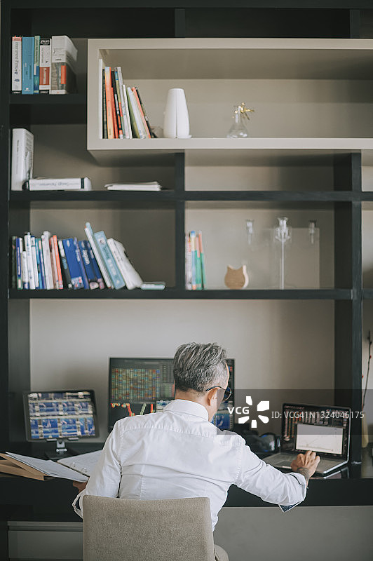 中国老年男子在家中工作，多台电脑监控股市图片素材