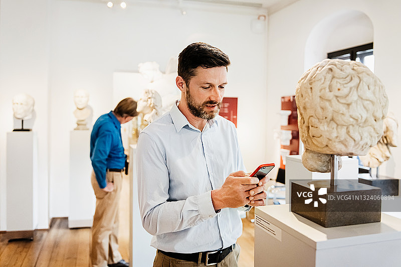 参观者在博物馆使用智能手机观看古典展览图片素材