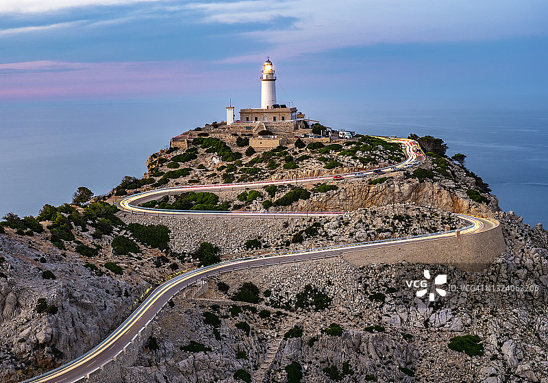 马略卡岛日落时分通往福门托角灯塔的弯曲道路上的车灯轨迹俯视图图片素材