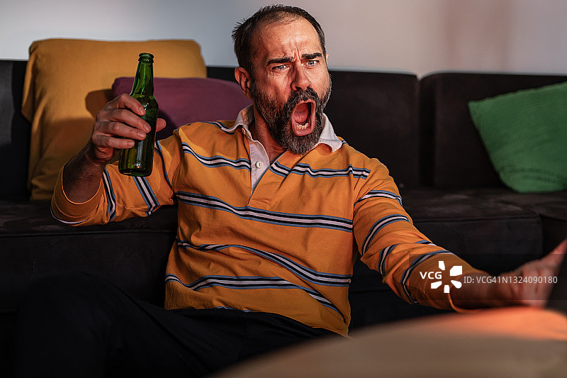 中年男人喝啤酒看电视体育比赛图片素材