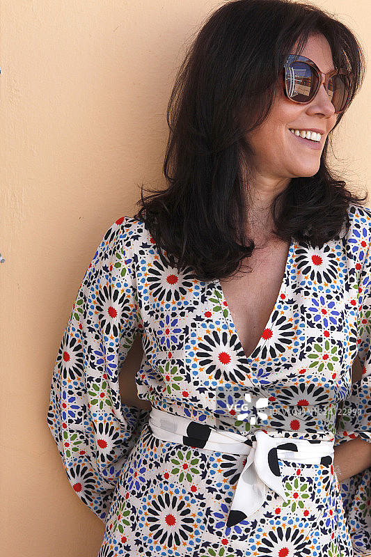 拉丁裔女人戴着太阳镜，穿着印花连衣裙，微笑并看向别处图片素材