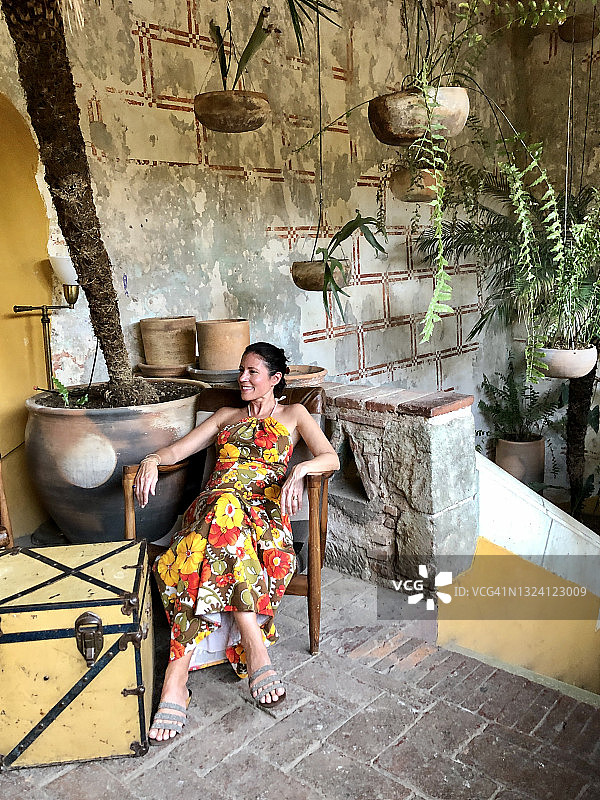 穿着复古连衣裙坐在传统装饰大厅的复古椅子上的女人图片素材