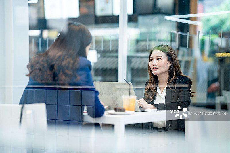 两位亚洲女商人穿着得体的西装在咖啡馆外认真地谈论工作图片素材