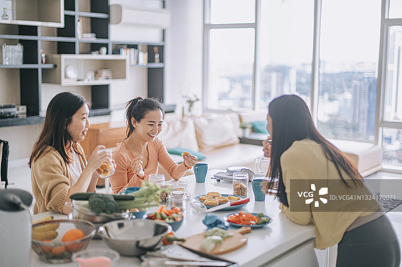 三位中国亚洲女性朋友周末在家中厨房柜台享用早餐图片素材