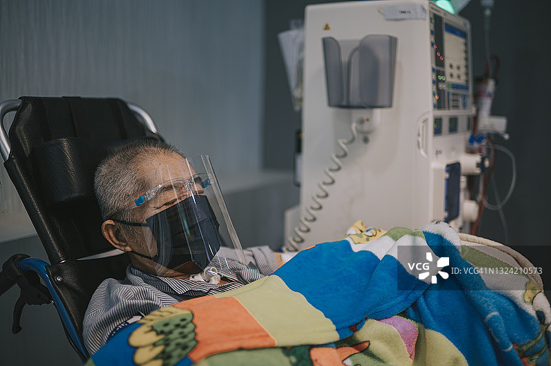 在医院接受透析治疗的华人老年男人，戴着面罩和防护面罩坐在轮椅上图片素材