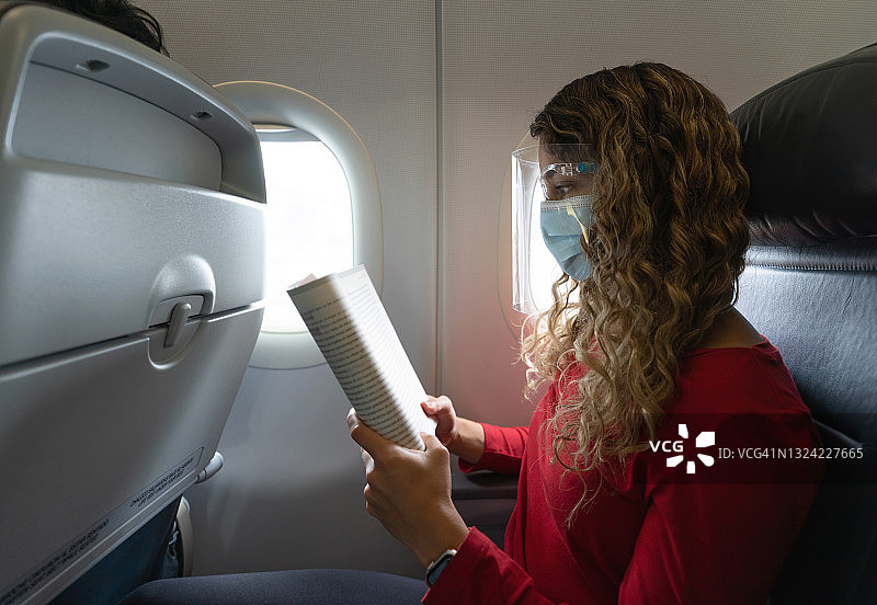 戴着口罩和防护面罩阅读的飞机乘客图片素材