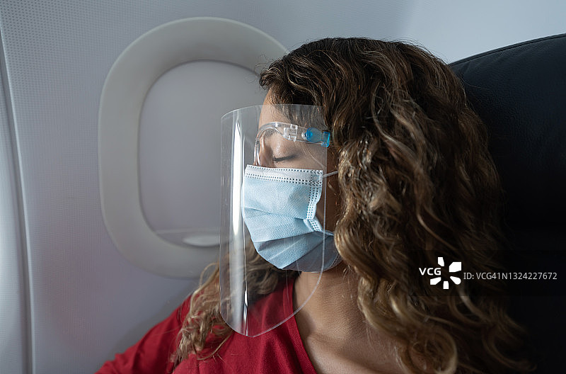 在飞机上戴口罩和防护罩睡觉的女人图片素材