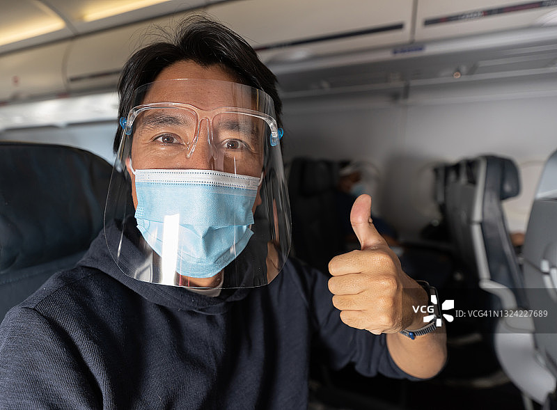 在飞机上戴着口罩和防护面罩，竖起大拇指的男人图片素材
