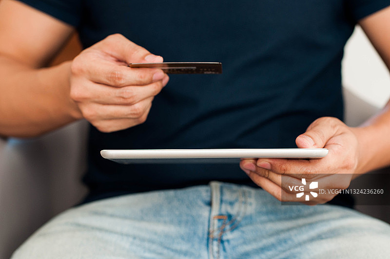 年轻的东南亚男子将信用卡同步到平板电脑图片素材
