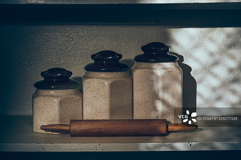 三个陶瓷食品储藏罐和一个在食品储藏室架子上的擀面杖图片素材