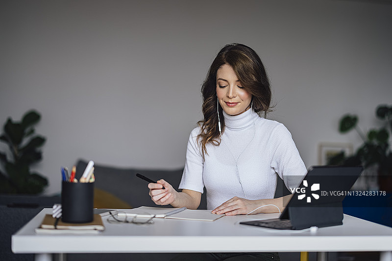 在家工作：使用平板电脑做笔记的年轻女商人图片素材