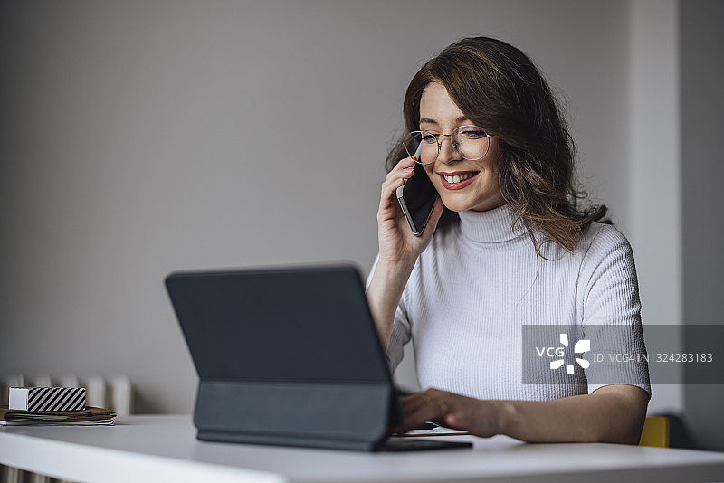 居家办公：戴眼镜的年轻女商人拿着手机看电脑图片素材