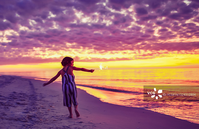 在迷人海滩日落时玩烟花棒的儿童，童年的快乐和自由图片素材