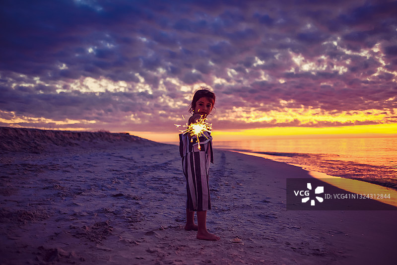 在迷人海滩日落时玩烟花棒的儿童，童年的快乐和自由图片素材