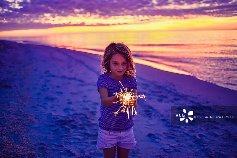 在迷人海滩日落时玩烟花棒的儿童，童年的快乐和自由图片素材