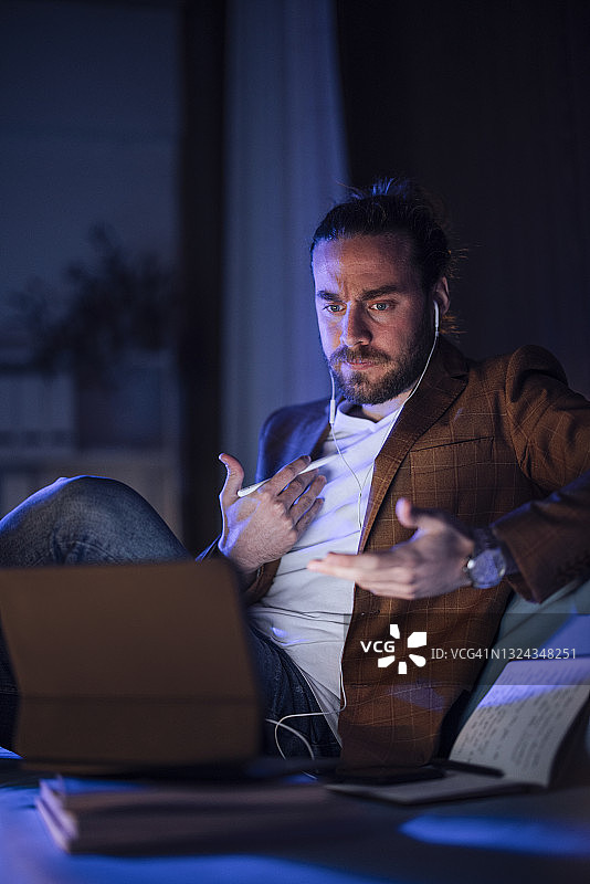 深夜在家工作：专注的商务男士戴着耳机握笔图片素材