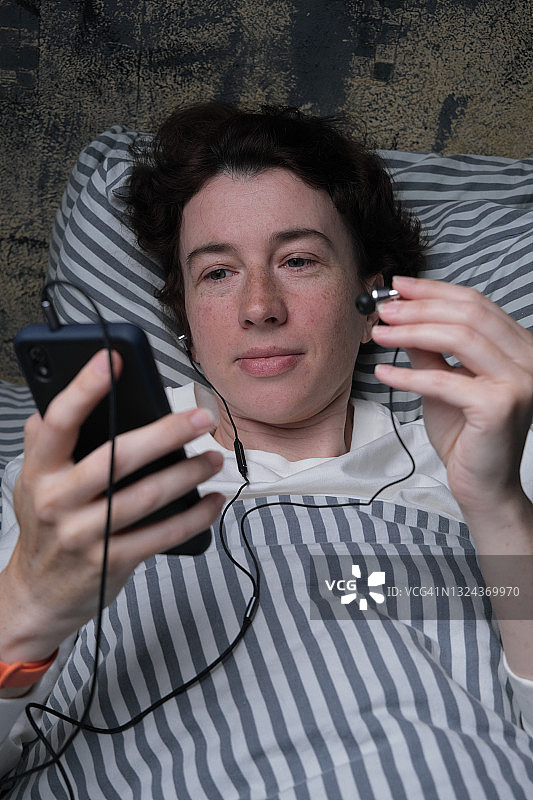 躺在床上戴着耳机听音乐的中年妇女图片素材