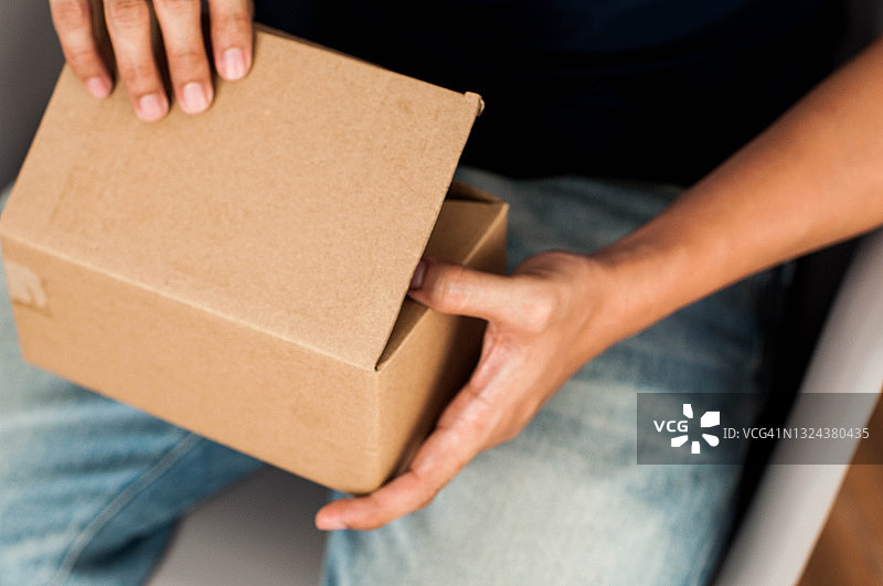 一名东南亚男子在室内打开一个小型纸箱包裹图片素材