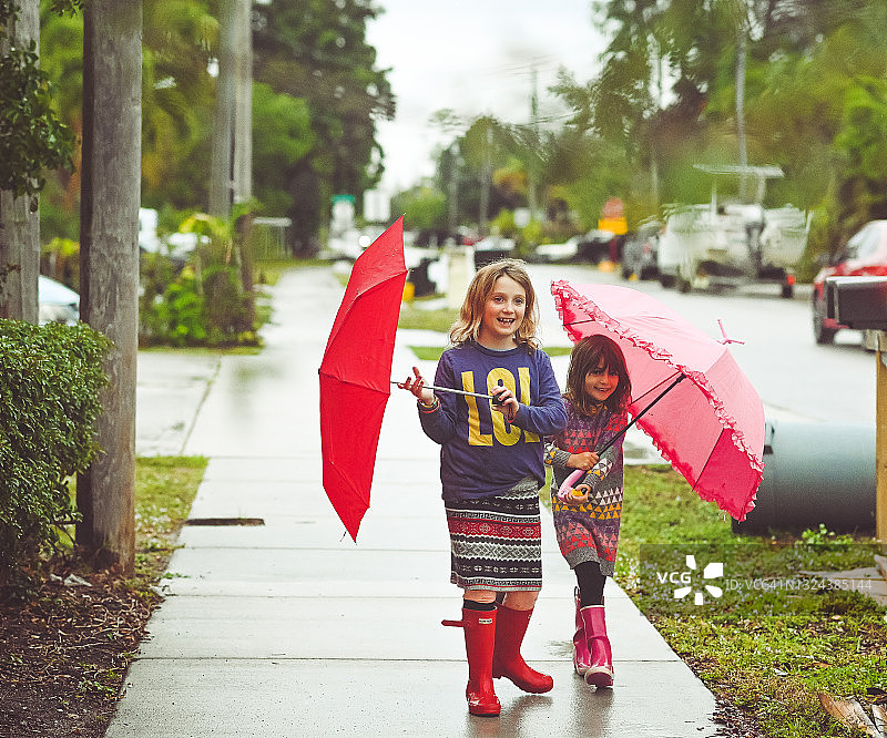 穿着雨靴和拿着雨伞的彩色儿童在雨天户外玩耍图片素材