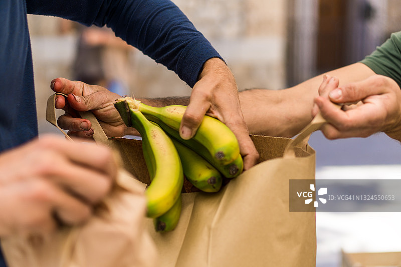 水果商贩帮助顾客将香蕉装入再生纸袋图片素材