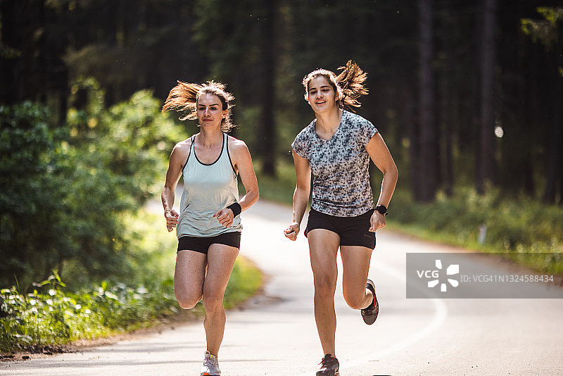 两位年轻女运动员在森林的道路上慢跑图片素材