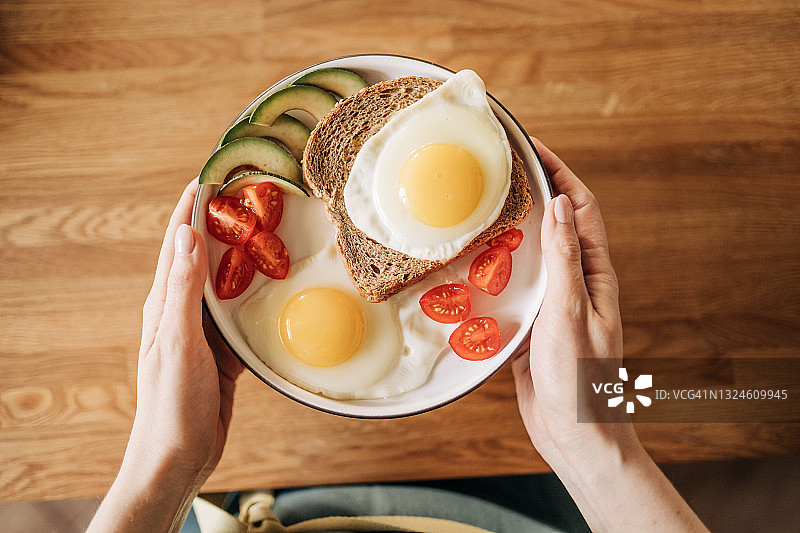 女孩在煎锅上方放入三个鸡蛋，配以香草、奶酪和西红柿，制作早餐图片素材
