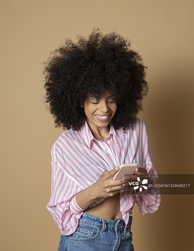 在米色背景下使用手机的非洲混血女人图片素材