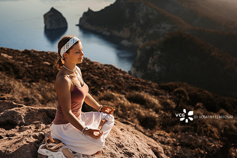 年轻女人在山区海景的黄金时段，以智慧手印闭目冥想图片素材